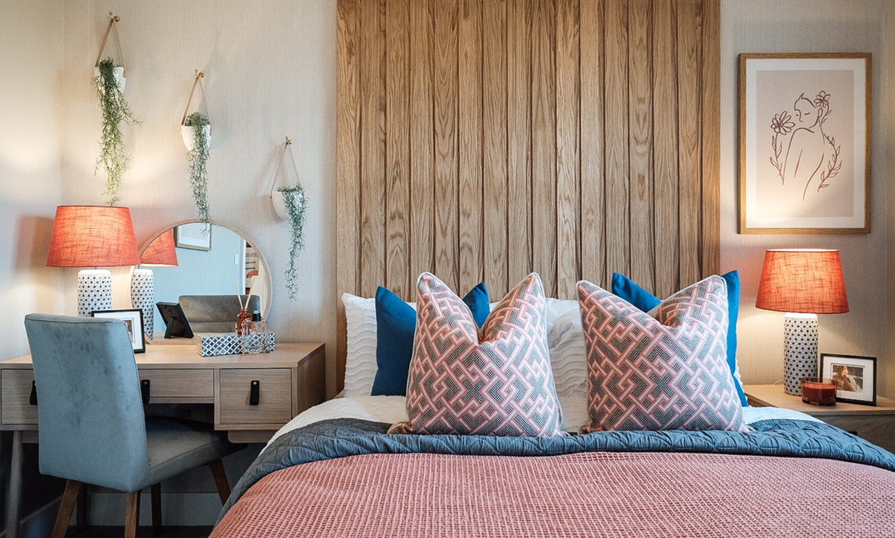 A double bedroom decorated in pastel colours with wooden panelling behind the bed and a desk in the corner