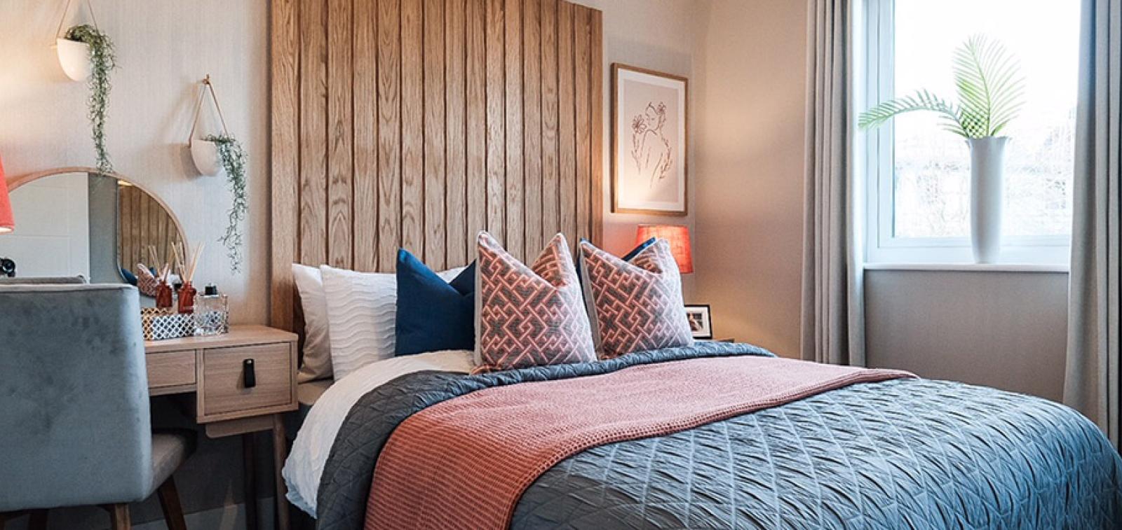 An example of an interior designed bedroom with floor to ceiling wooden slat headboard and pink and grey bedding.