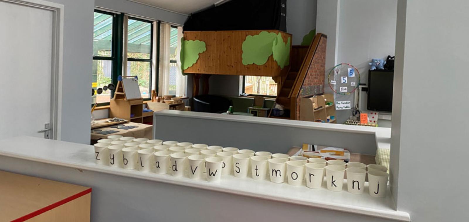 A kitchen in a classroom showing multiple plastic cups with a large letter on the front of each