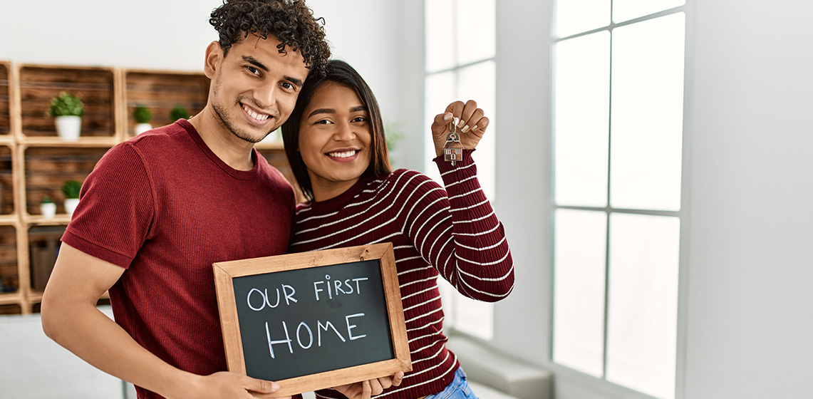 Two people holding a chalkboard saying our first home and holding keys