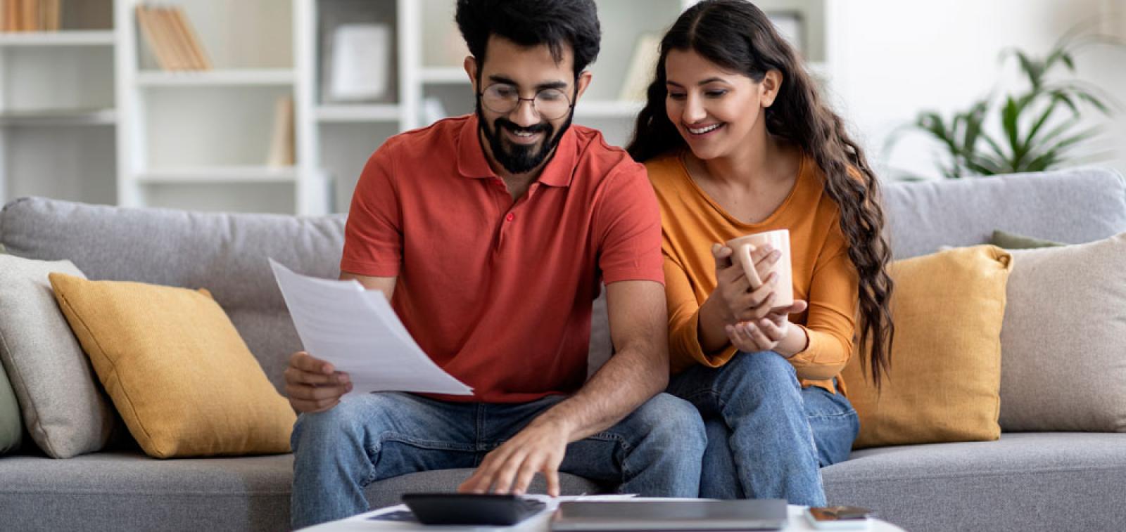 Two people sat on a sofa reading through some paperwork