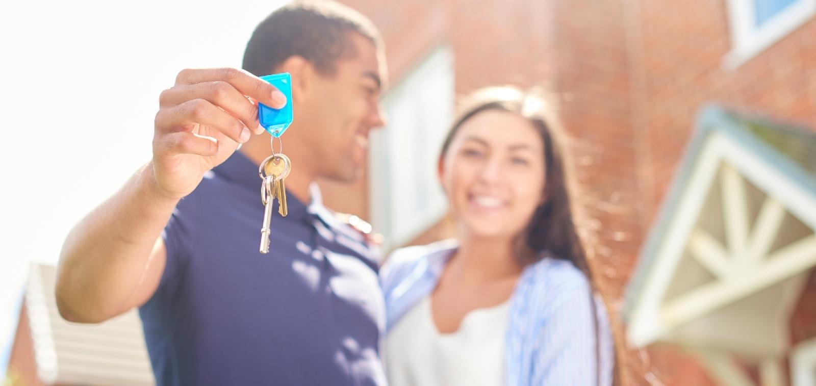 A couple stood outside a house in an embrace holding keys