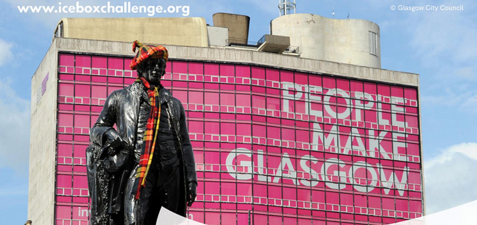 A large multistorey building in Glasgow with the windows covered pink with large writing that reads people make Glasgow. A statue of a man wearing a hat and scarf stands in the forefront