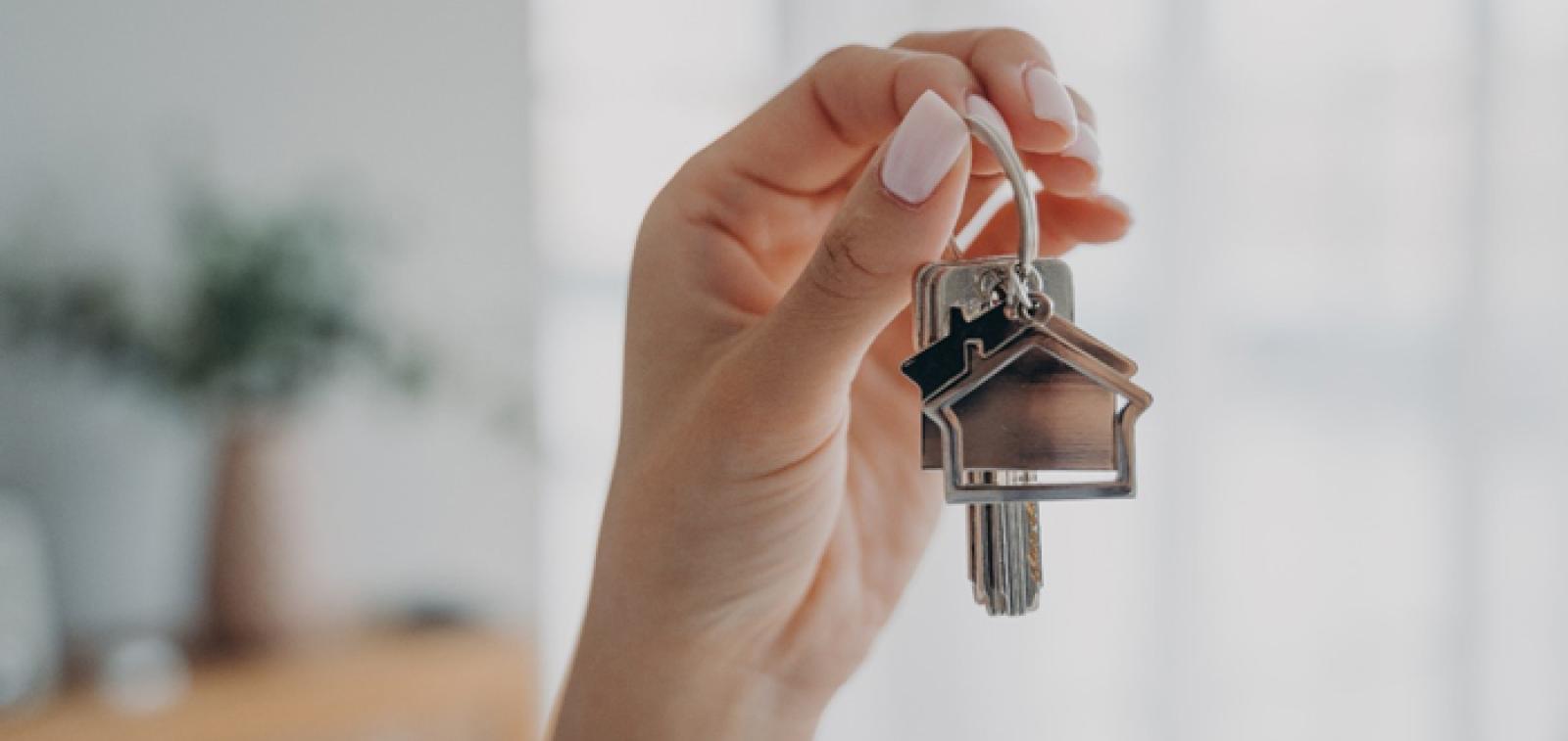 A set of keys with a house keyring behind held up by a hand