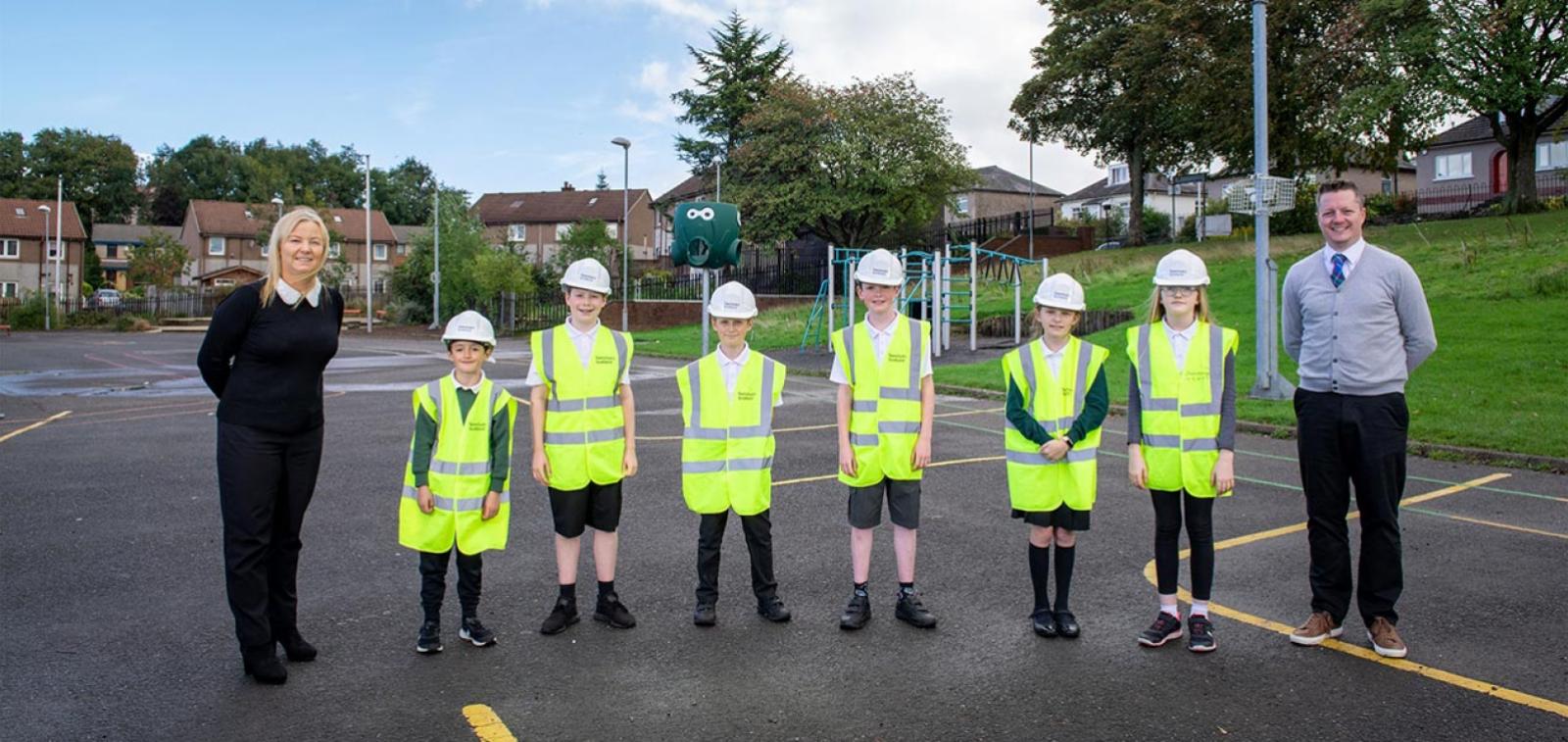 6 children dressed in high visibility vests alongside two adults stood on a playground