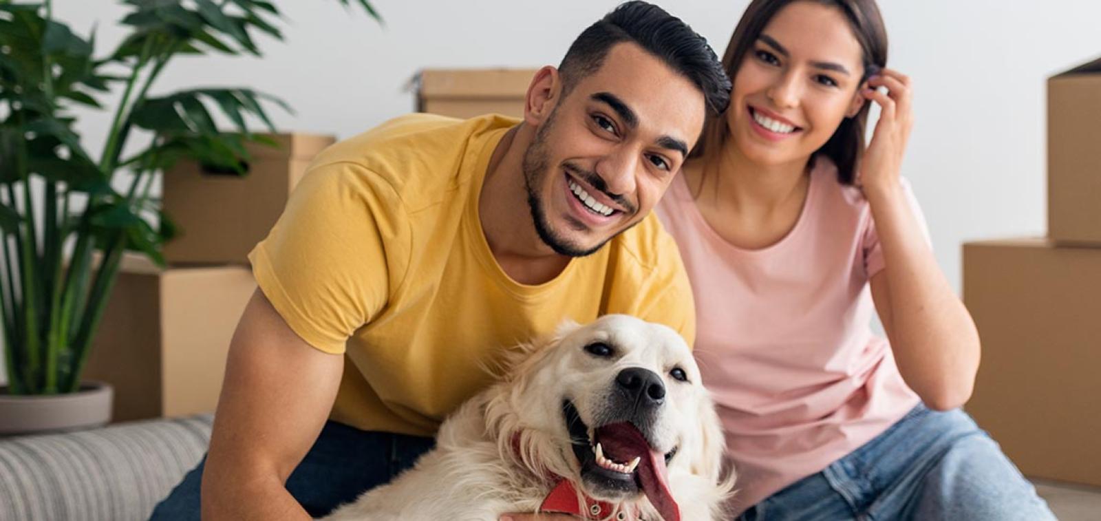 Two people sat with a dog in front of moving boxes