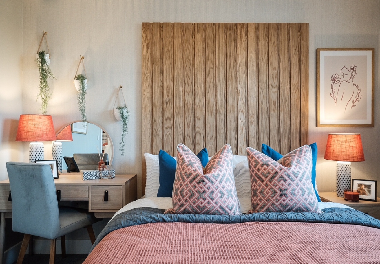 A double bedroom decorated in pastel colours with wooden panelling behind the bed and a desk in the corner