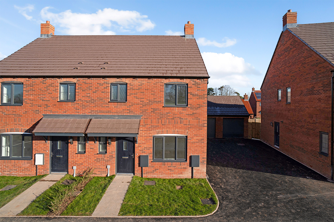 A red brick semi-detached house with a shared garage an tarmacked driveway