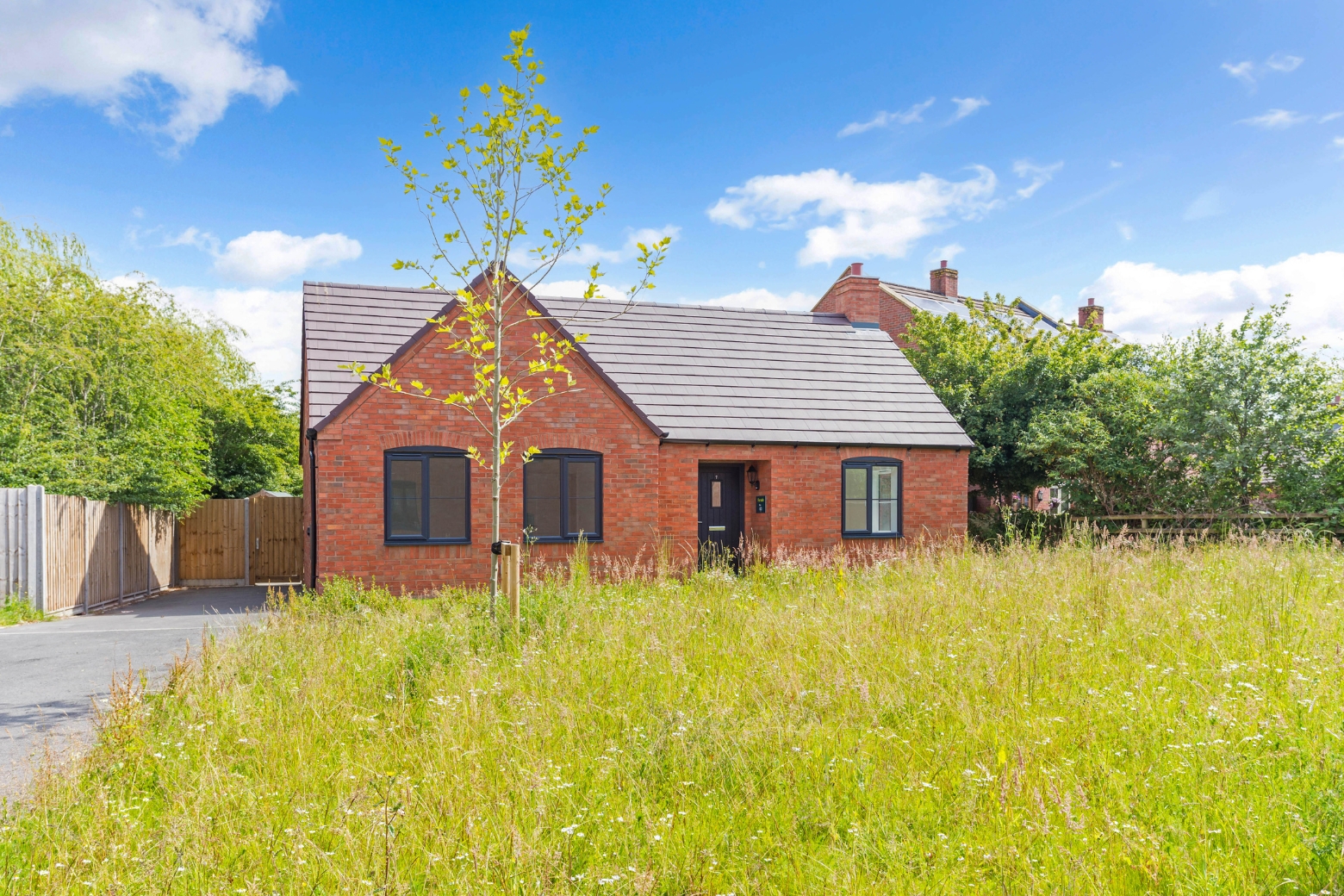 A red bricked bungalow at the end of a long drive with a common grassed area in front