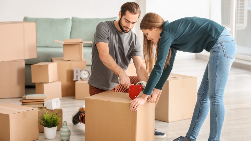 A couple in a room full of boxes taping them up preparing to move house