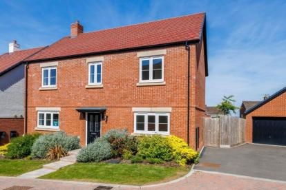Modern two-story detached brick home with red-tiled roof, white-framed windows, landscaped front garden, paved path, and driveway leading to a detached garage.