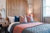 An example of an interior designed bedroom with floor to ceiling wooden slat headboard and pink and grey bedding.