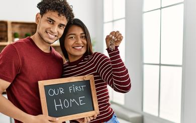 Two people holding a chalkboard saying our first home and holding keys