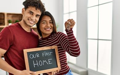 Two people holding a chalkboard saying our first home and holding keys