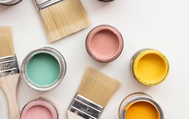 A collection of open paint pots of bright colours with several paintbrushes