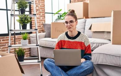 A person sat on the floor of their home after moving in, surrounded by moving boxes.