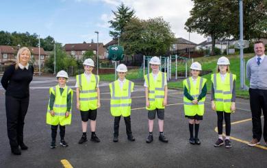 6 children dressed in high visibility vests alongside two adults stood on a playground