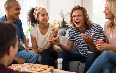 A group of friends laughing and eating pizza together