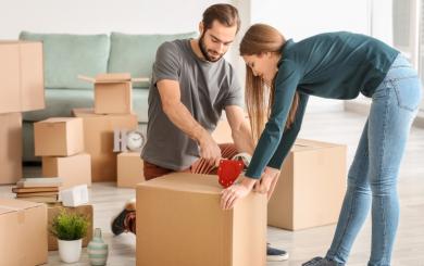 A couple in a room full of boxes taping them up preparing to move house