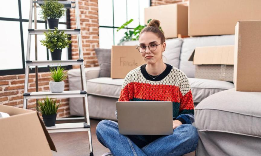 A person sat on the floor of their home after moving in, surrounded by moving boxes.