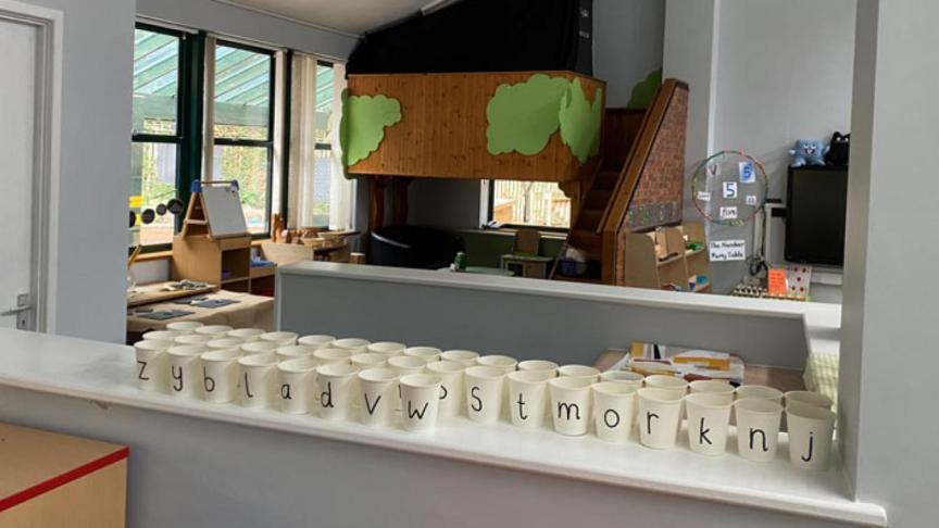 A kitchen in a classroom showing multiple plastic cups with a large letter on the front of each
