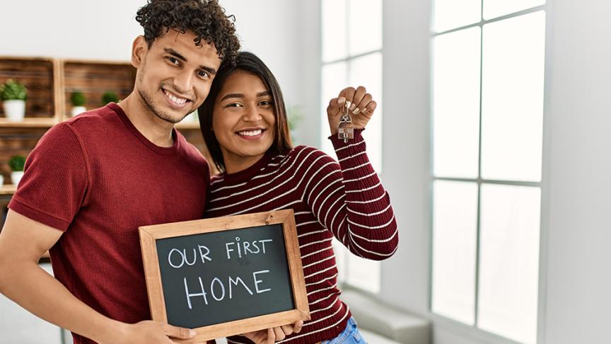 Two people holding a chalkboard saying our first home and holding keys