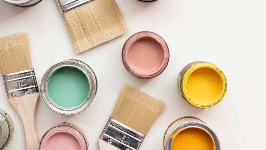 A collection of open paint pots of bright colours with several paintbrushes