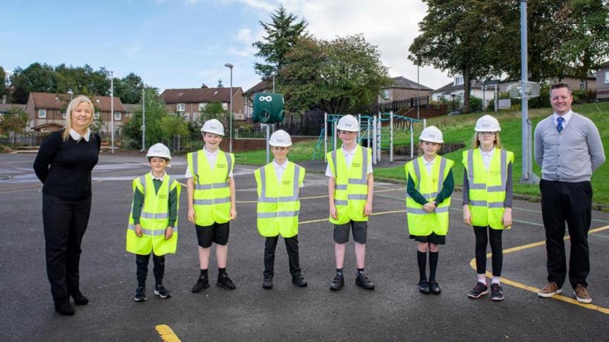 6 children dressed in high visibility vests alongside two adults stood on a playground