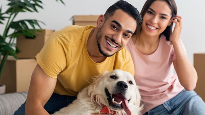 Two people sat with a dog in front of moving boxes 