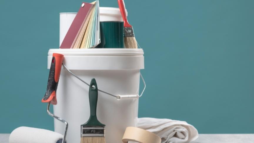 A tub of paint and paintbrushes against a newly painted blue wall