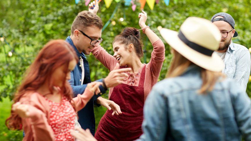 A group of men and women dancing in a garden decorated with multicoloured bunting.