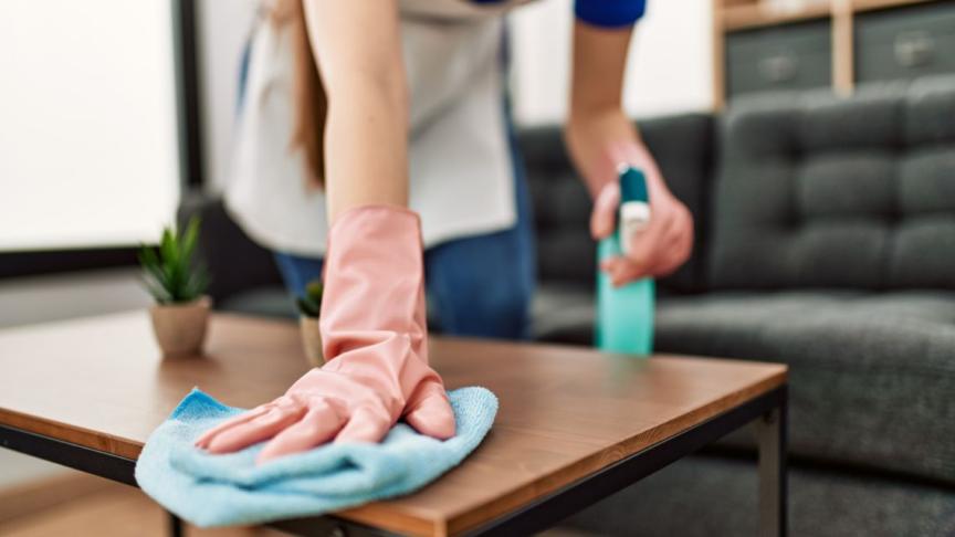 A person wearing rubber gloves and a cleaning spray bottle wiping down a coffee table
