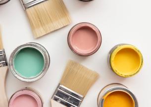 A collection of open paint pots of bright colours with several paintbrushes