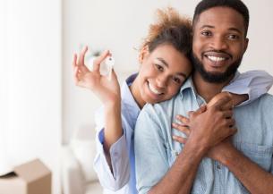 A male and female couple smiling at the camera, with the female holding up a key. She has her arm over the male in a sweet embrace