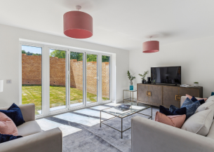 A new-build living room with white walls, patio doors leading to a sunny garden and stylish furniture inside